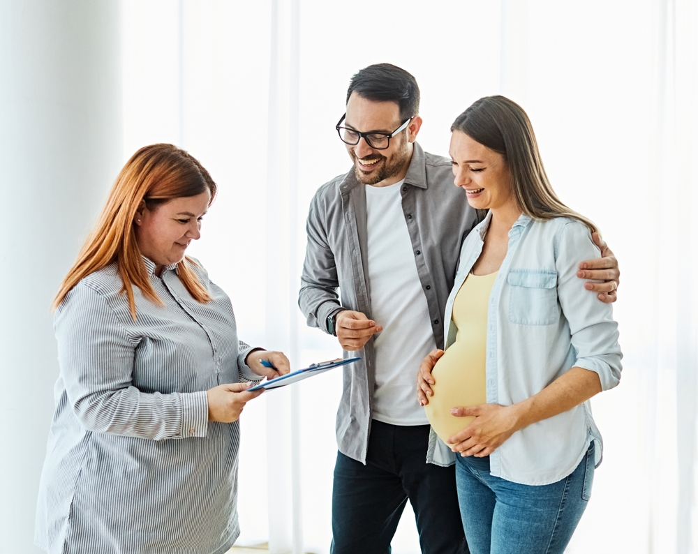 Young happy couple, a pregnant woman, and an agent in a new property