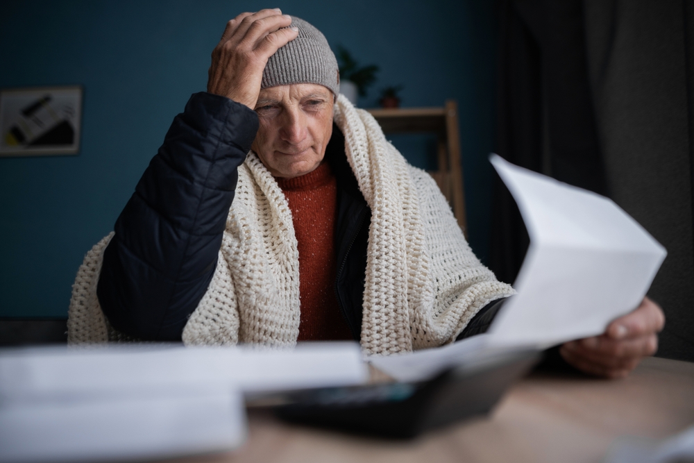 Frustrated poor bankrupt old man freezing at home with no money, holding heating bill, power cut notification letter. Copy space