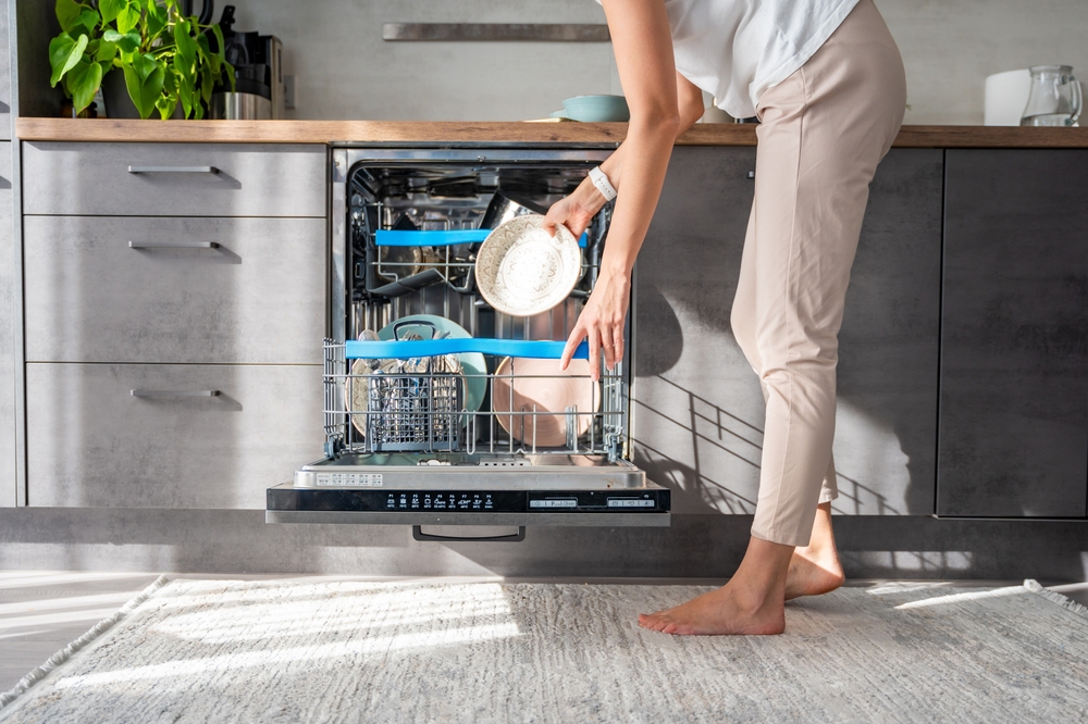Woman removes clean ceramic dishes from dishwasher. Household and useful technology concept. High quality photo