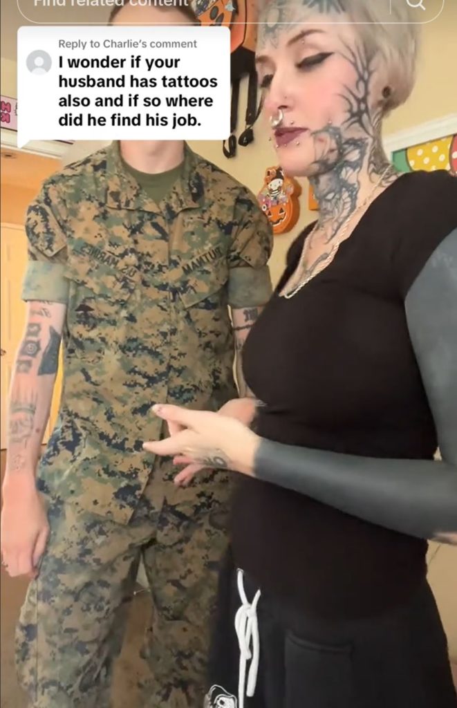 Woman with tattoos standing next to man with tattoos wearing military uniform. 