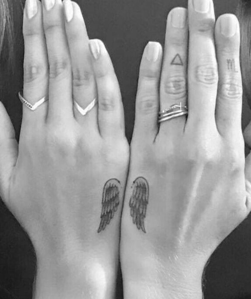 Gray image of hands with wing tattoos and rings