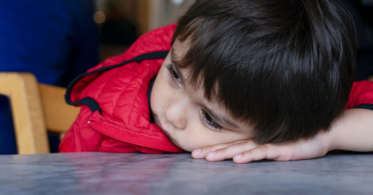 child in red jacket with head on hand on a table