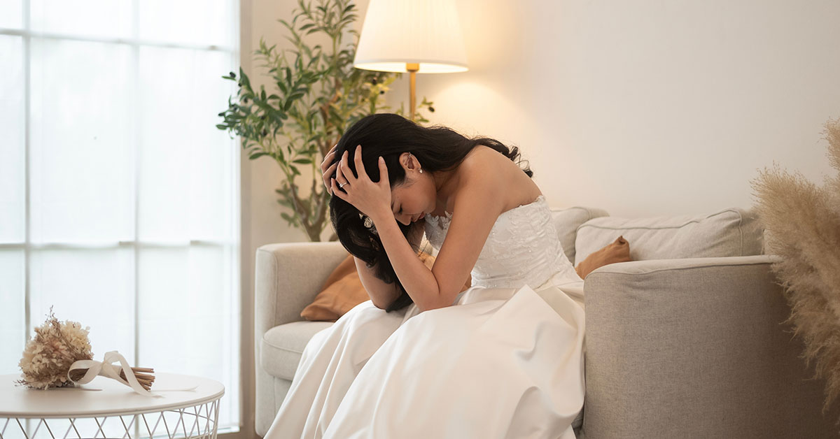 woman in wedding dress distraught sitting on couch with face in her palms