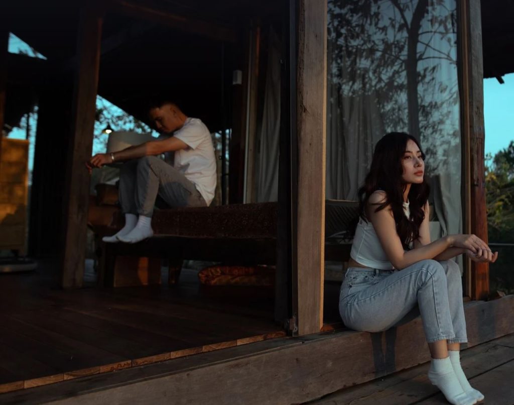Couple looking pensive, sitting apart from each other. Nature in the background.