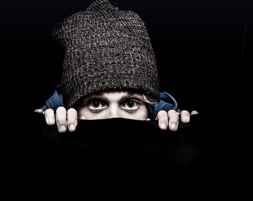 Person wearing a knitted hat only part of their face is visible. Surrounded by all black. 
