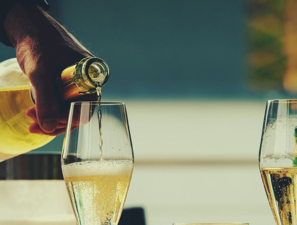 Hand pouring sparkling wine into a glass next to a half-full glass. Blurred background