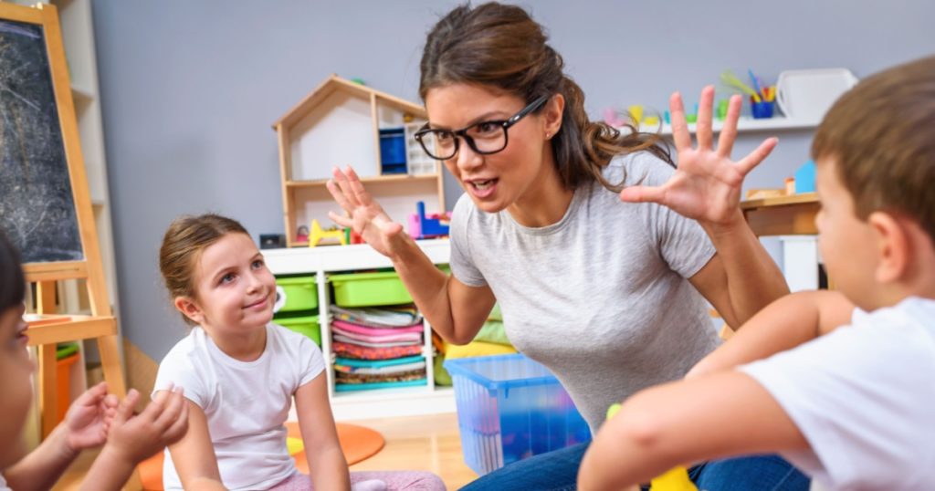 Preschool teacher talking to group of children sitting on a floor at kindergarten