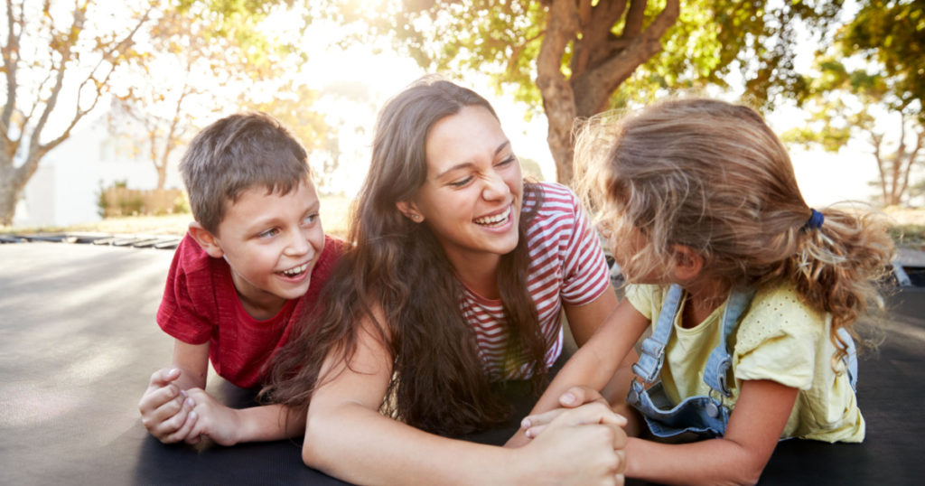 Siblings With Teenage Sister Playing On Outdoor Trampoline In Garden