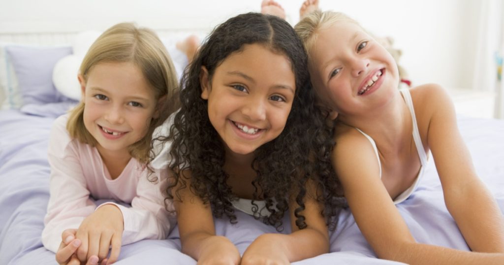Three Young Girls Lying On A Bed In Their Pajamas