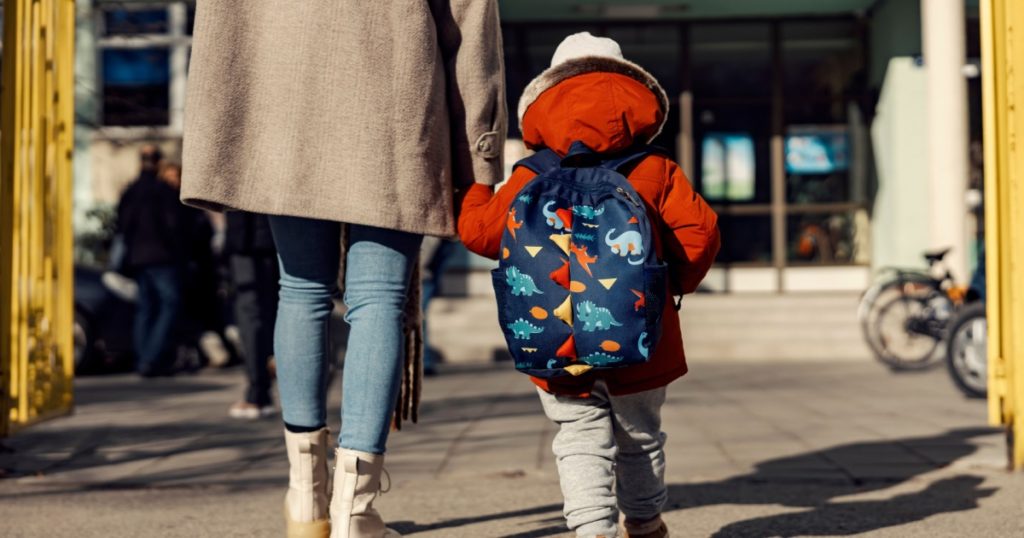 A mother entering the kindergarten yard with her preschooler boy.