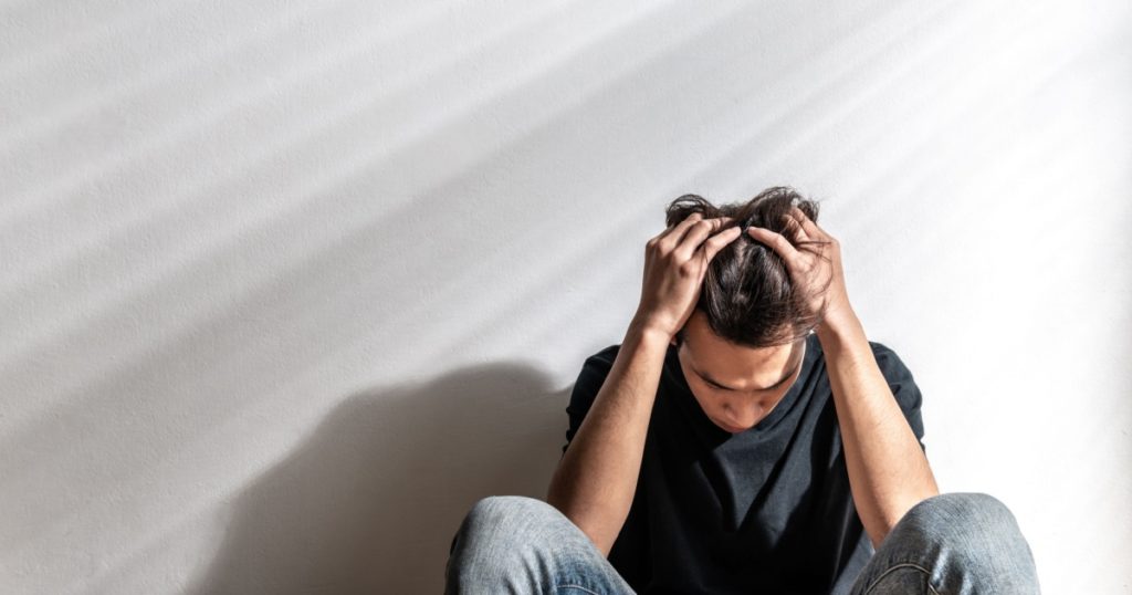Male depression. Upset Asian young man having problems over white background, having heavy thoughts, break up with lover or financial difficulties