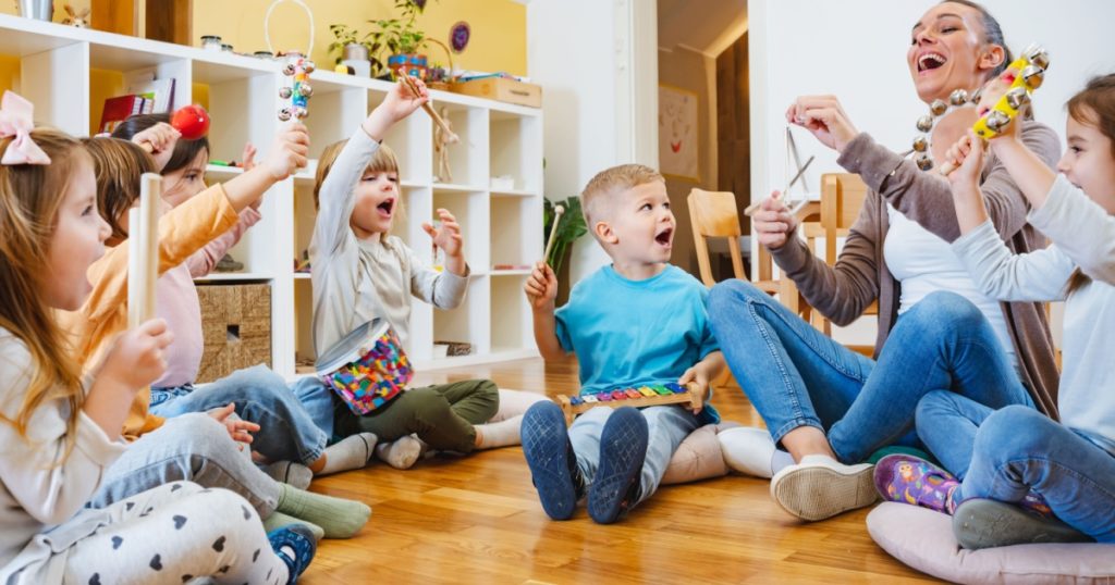 Kindergarten teacher with children sitting on the floor having music class, using various instruments and percussion. Early music education