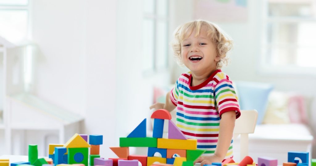 Kid playing with colorful toy blocks. Little boy building tower of block toys. Educational and creative toys and games for young children. Baby in white bedroom with rainbow bricks