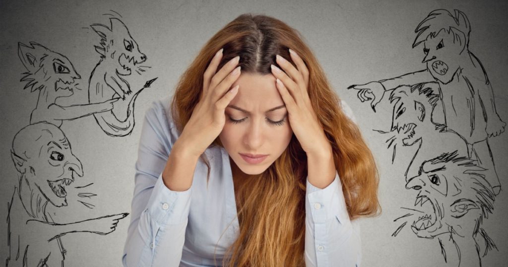 Evil Men pointing at stressed woman. Desperate young businesswoman sitting at desk in her office isolated on grey wall background. Negative human