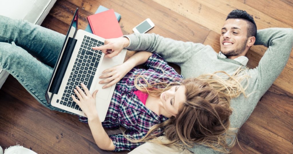 Couple shopping online at laptop computer - Two young friends watching a video on a notebook in the living room, view from above
