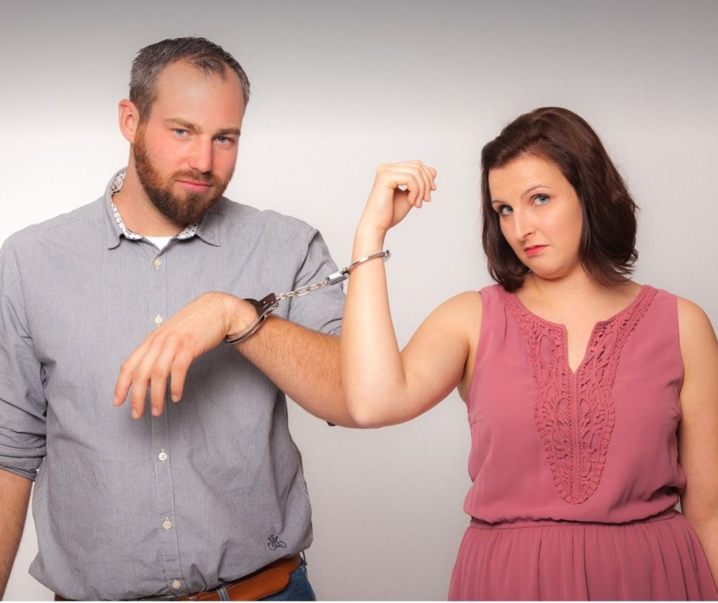 Man and woman handcuffed to each other. White background. 
