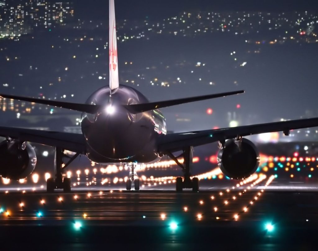 Airplane landing on runway at night. City lights in the background. 