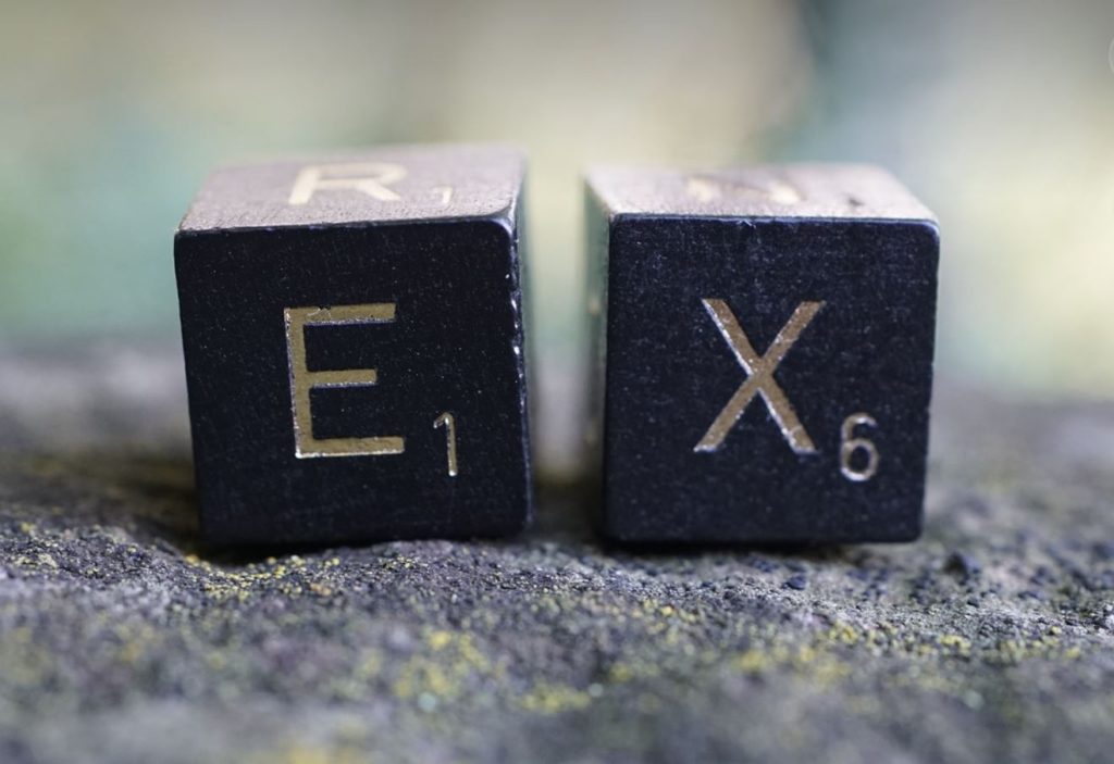 Scrabble letters spelling out "ex" on a stone wall. Blurred background. 
