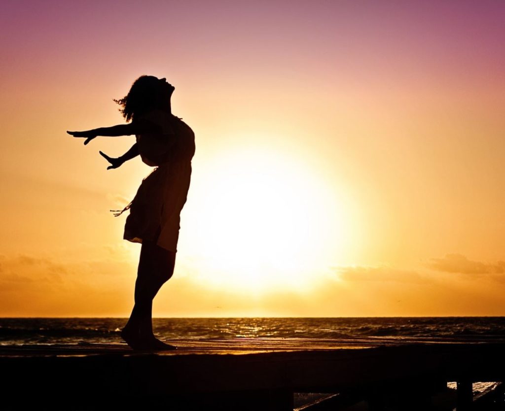 Silhouette of a woman with a sunset and the ocean in the background.