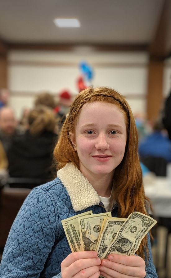 Red headed girl holding money blurred people and white wall with wooden beams in the background. 