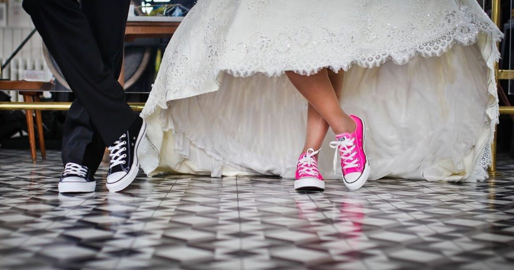 Bride and groom wearing pink and black converse, respectively. Balck and white checkered floor. 