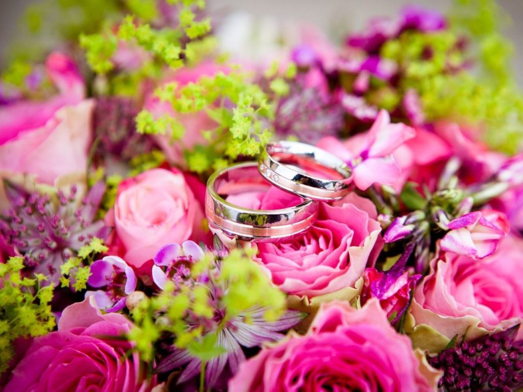 Pink bouquet of flowers with two wedding bands on top. 