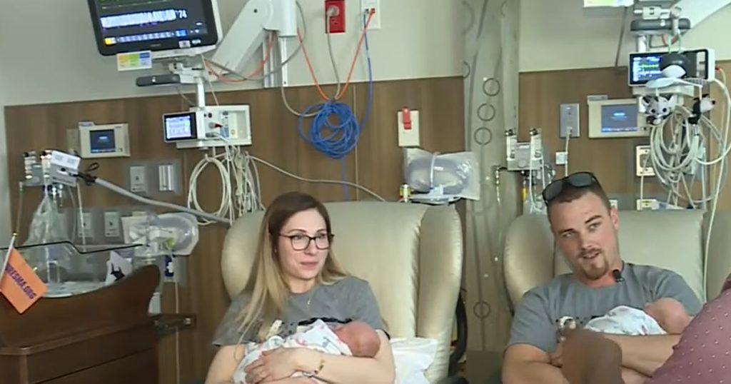 Parents hold newborns in a hospital room. Hospital equipment in the background.