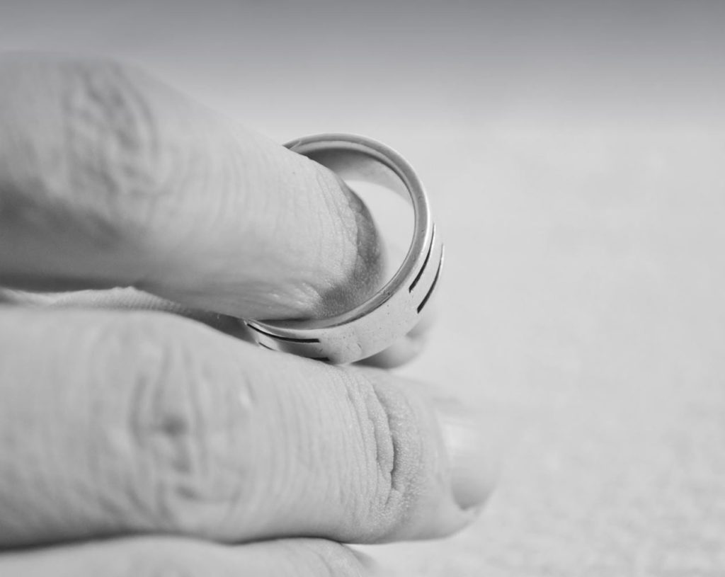 Black and white photo of a hand holding a wedding band. 