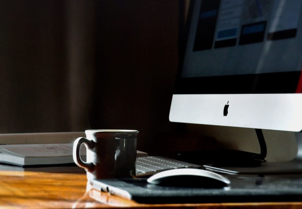 Workspace with a coffee cup and computer. Book and wooden desk in the background.