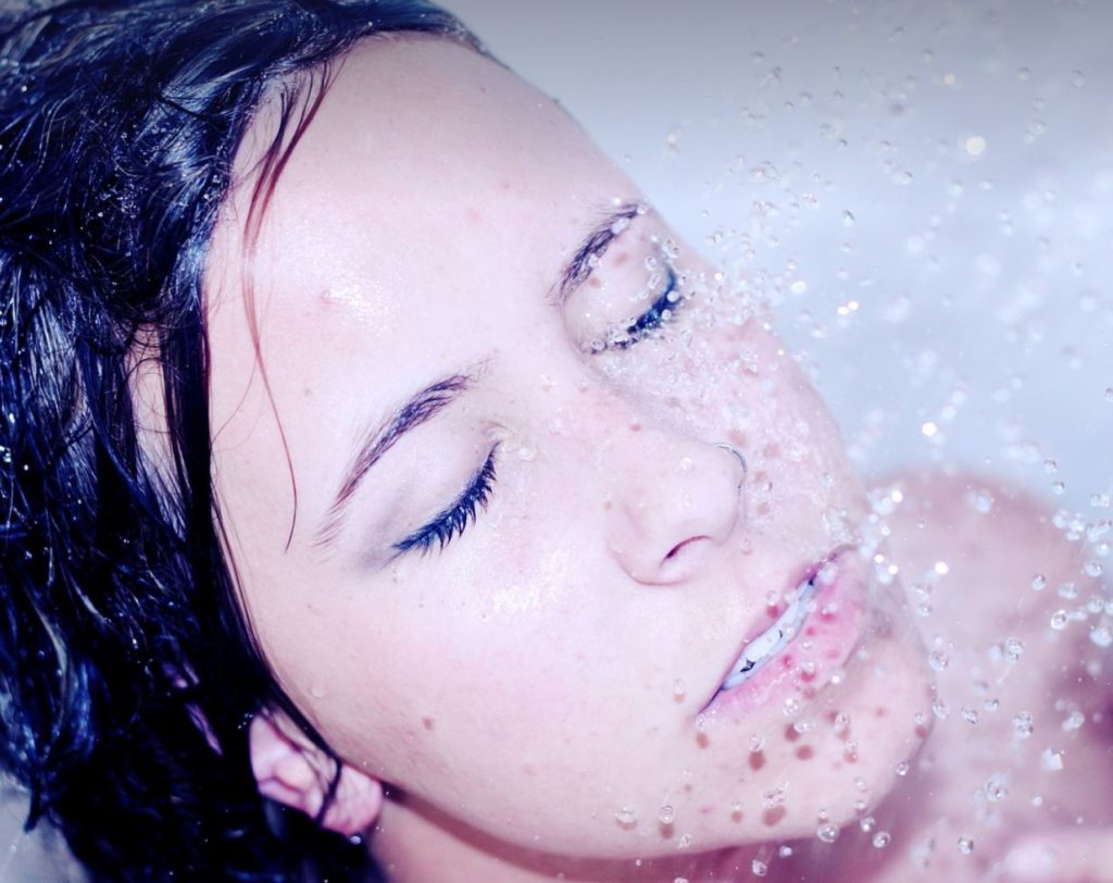 Close up of dark-haired woman's face with her eyes closed and water splashing down. 