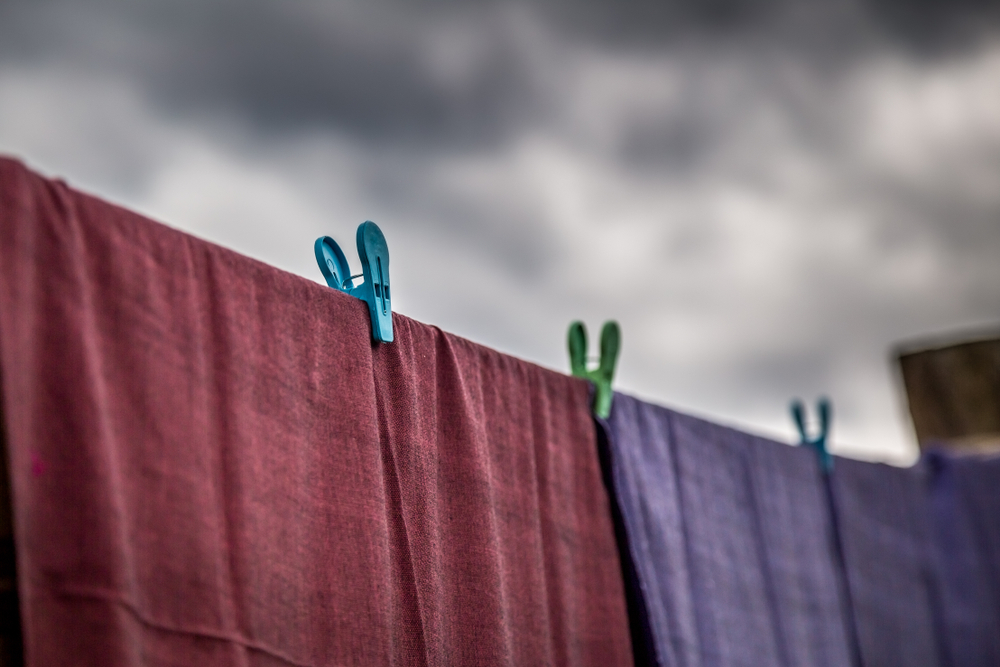 Clothing that has recently been washed is hung along the line to dry on clothes line with plastic clothespin with raining black cloud and storm coming
