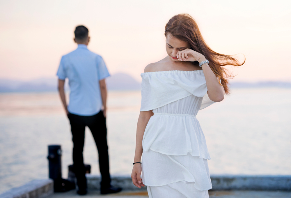 Young couple break up at the sea deck. Girl crying and walk away from man in concept love hurts,hard relationship,sad love story,when love is ended. Broken heart syndrome. How to fix a broken heart.