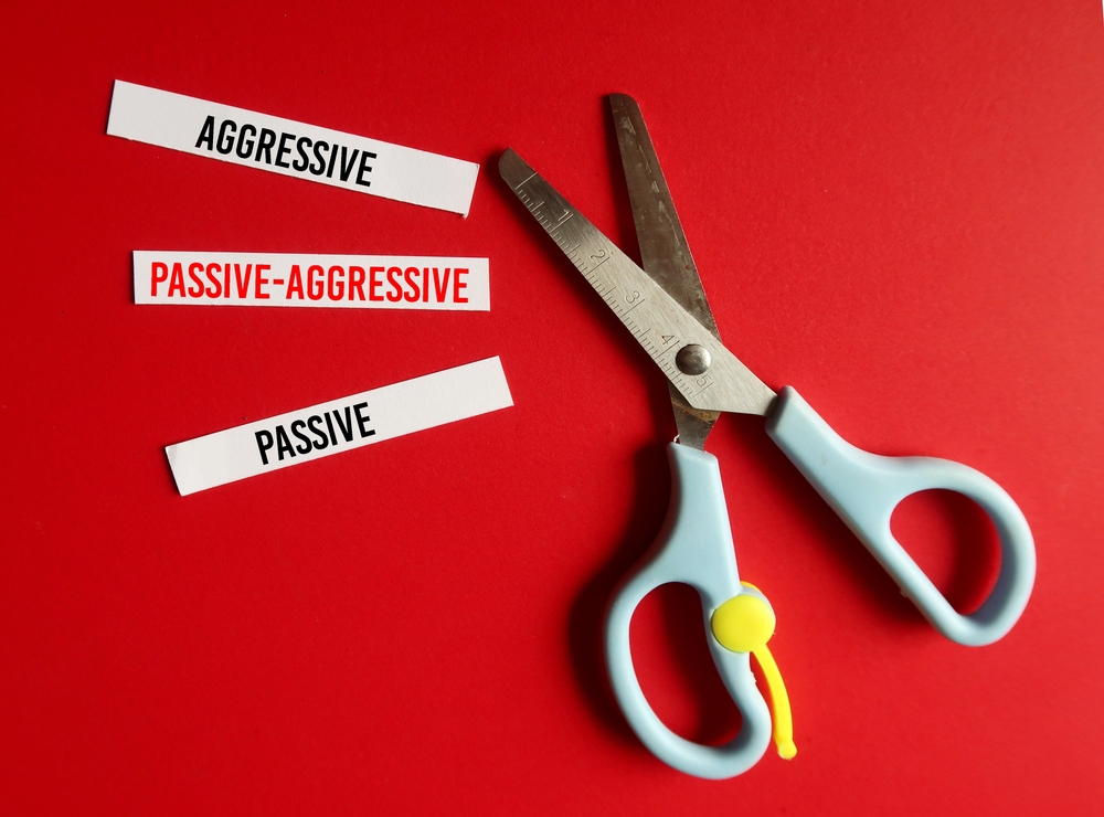 On red background, scissors and cut paper with text AGGRESSIVE, PASSIVE and highlight on PASSIVE AGGRESSIVE - pattern of indirectly expressing negative feelings instead of openly addressing them
