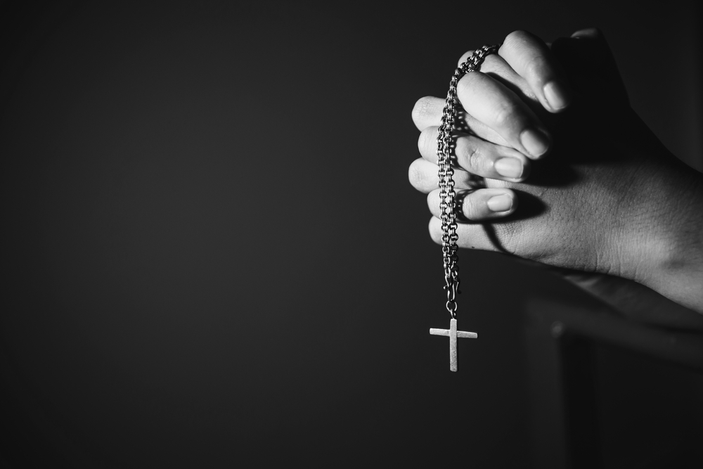 Image black and white woman hand holding rosary against cross and praying to God at church.