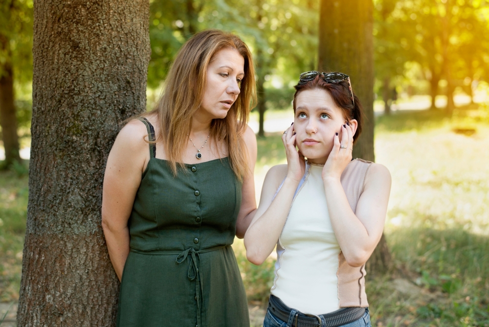 The teenage girl got tired of listening to her mother and closed ears, the girl constantly hears criticism and notations from her parents. Mother and teenage daughter are talking in the park