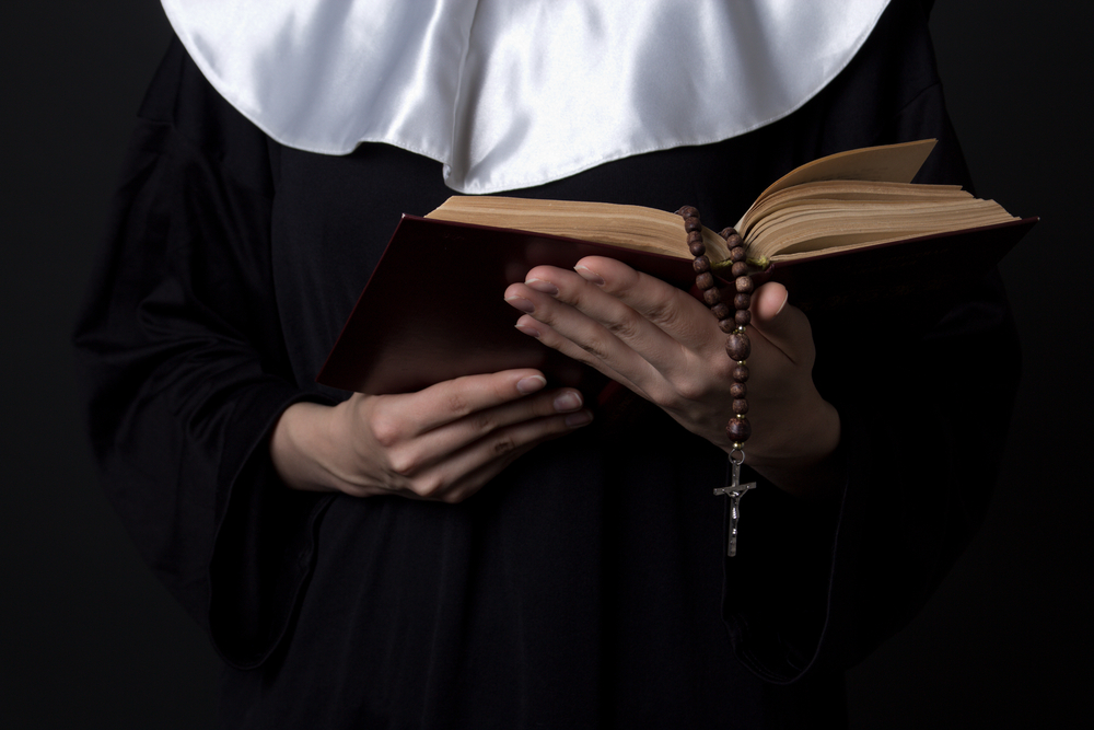 nun hands holding bible book over grey background