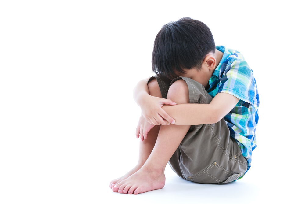 Little sad boy bare feet sitting on floor. Isolated on white background. Negative human emotions. Conceptual about children who lack warmth and affection, abandoned children. Free form copy space.
