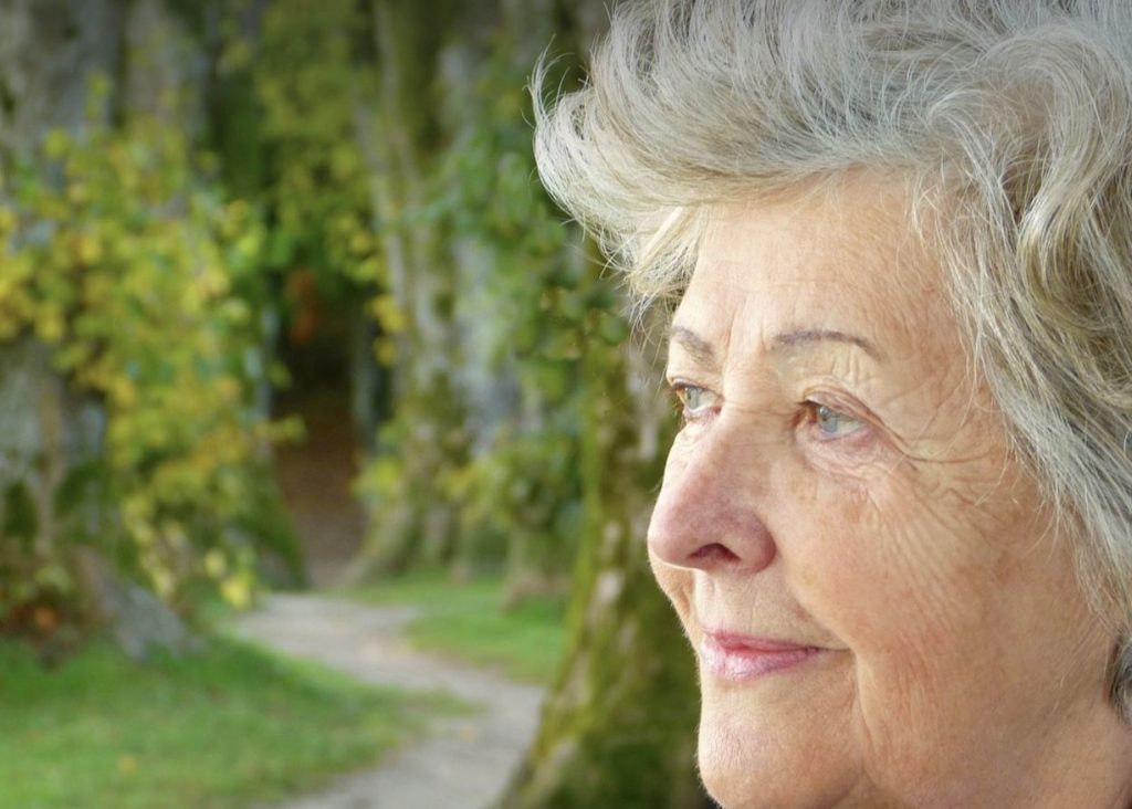 Close up of a woman pondering. Greenery in the background. 