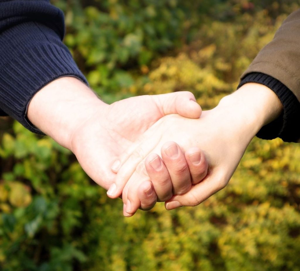 Couple holding hands, fall foliage in the background. 