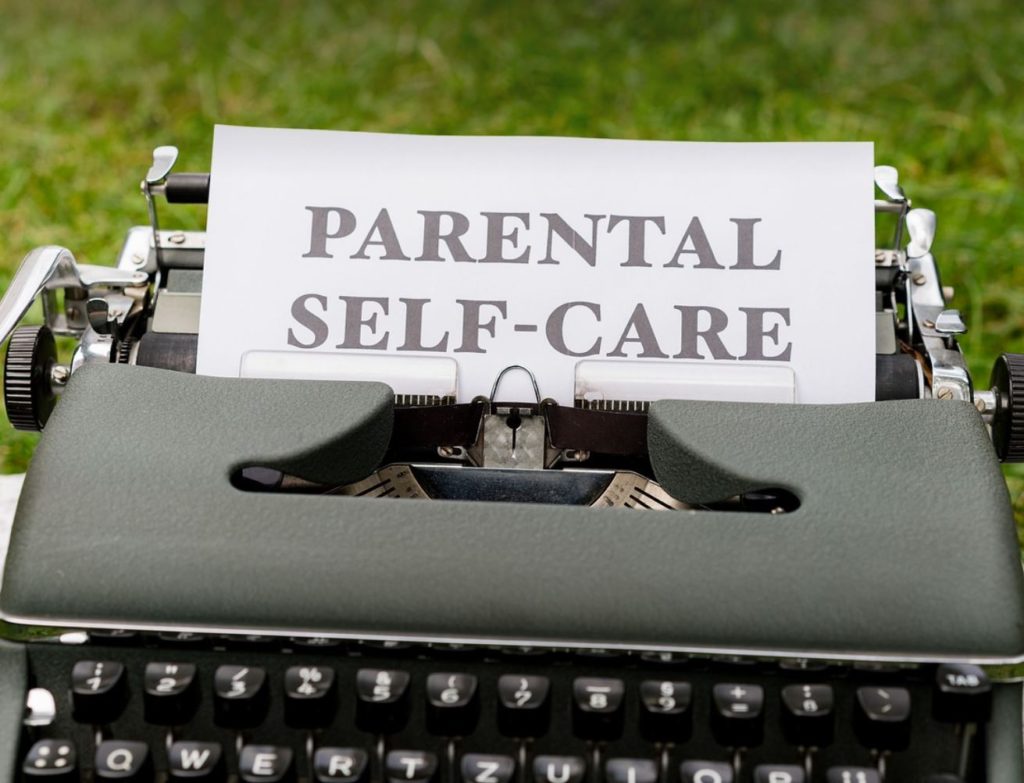 Old typewriter with the words parental self-care. Grass in the background.