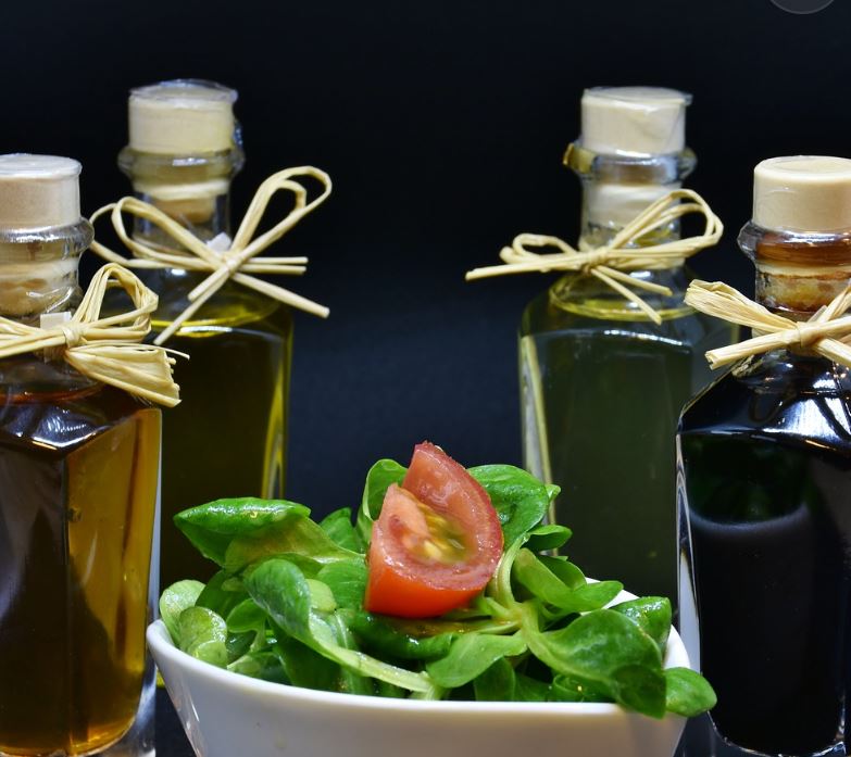 Four bottles of different color vinegar with a bowl of greens and a tomato slice. 