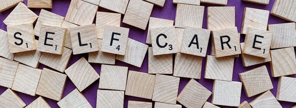 Scrabble tiles spelling self-care. Tiles and purple background. 