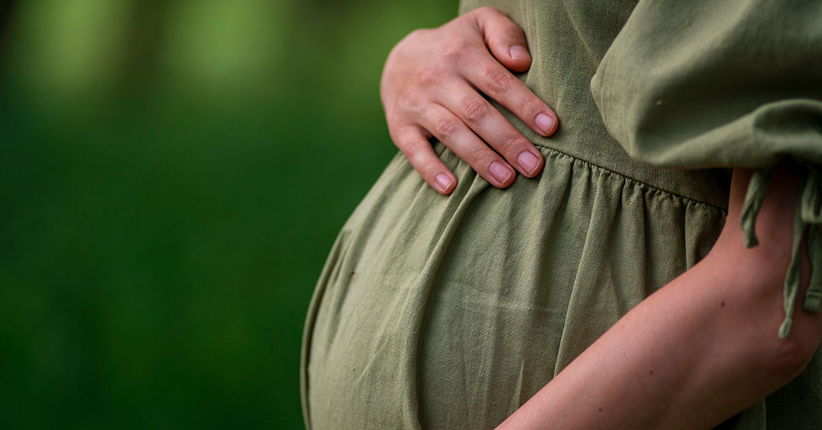 woman wearing green dress with hand placed on pregnant belly / baby bump