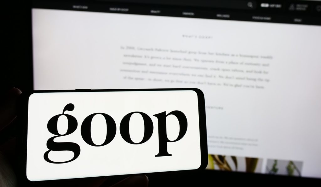 Person holding smartphone with logo of US publishing and e-commerce company Goop Inc. on screen in front of website. Focus on phone display. Unmodified photo.