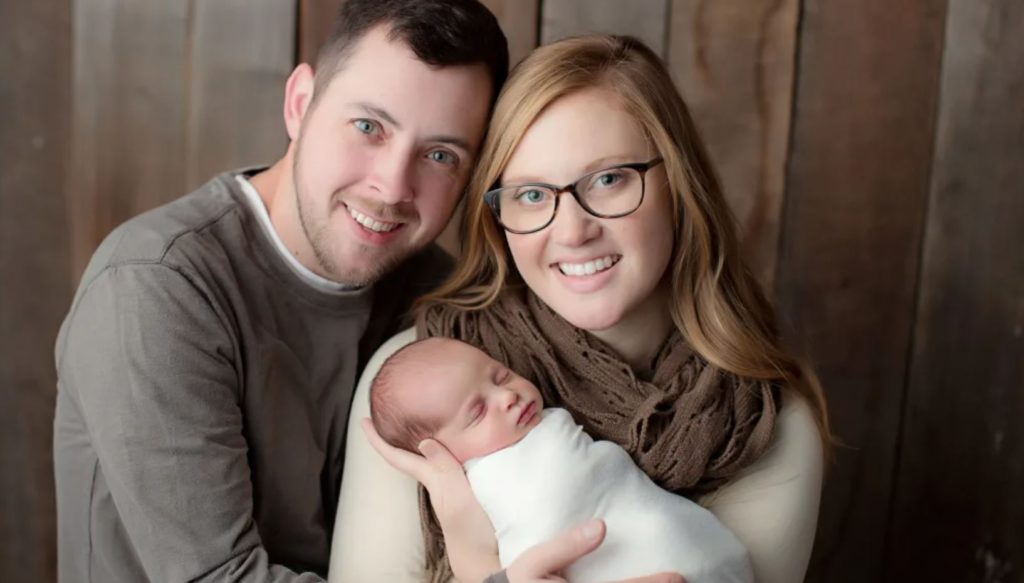 Happy parents posing with their new baby against a dark wooden background. 