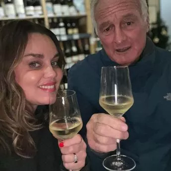 Man and woman side by side, holing wine glasses. Wine racks in the background. 