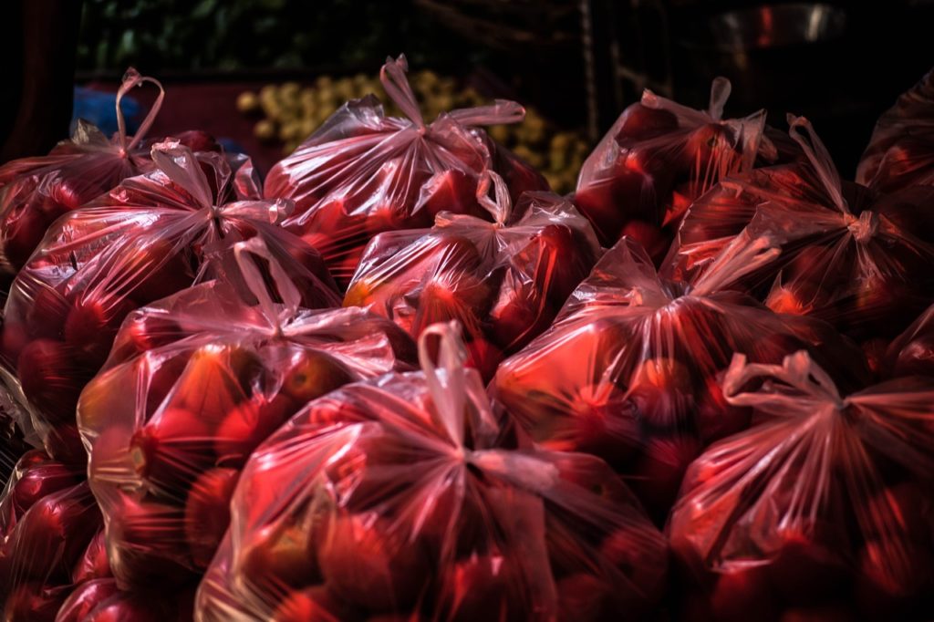 Red plastic bags filled will apples or tomatoes.