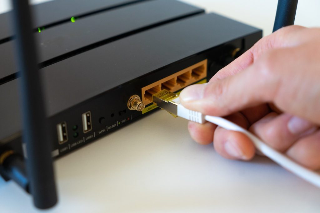 Una mano conectando un cable a un enrutador de Internet. Fondo blanco.