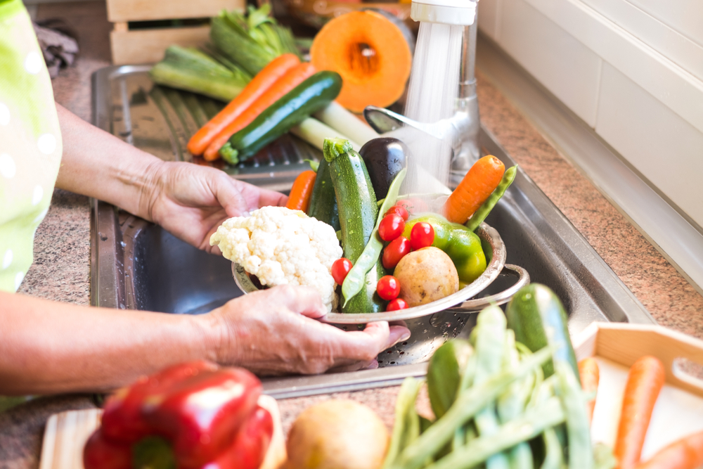 Washing vegetables in the kitchen. Hands of a senior woman cleaning an assortment of fresh and raw vegetables. A healthy diet rich in vitamins. Special for vegan and vegetarian people