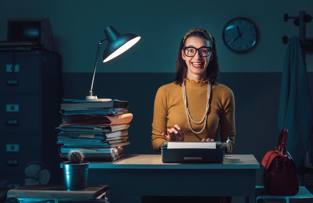 Efficient vintage style secretary working with a typewriter in the office and smiling at camera